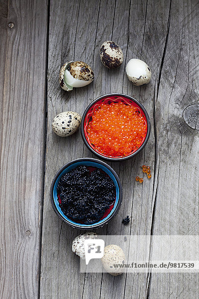 Schwarzer und roter Kaviar in Schalen,  gekochte Wachteleier auf Holz