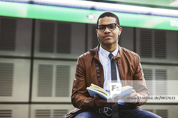 Spain  Barcelona  businessman sitting at underground station platform with book