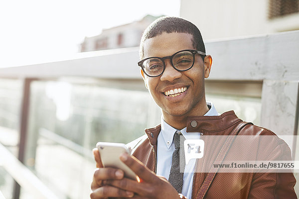 Porträt eines lächelnden Geschäftsmannes mit Smartphone in Lederjacke und Brille