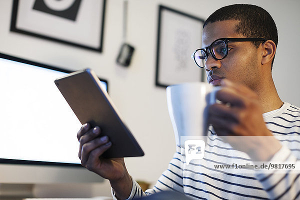 Junger kreativer Mann mit Mini-Tablette bei einer Kaffeepause in seinem Home-Office