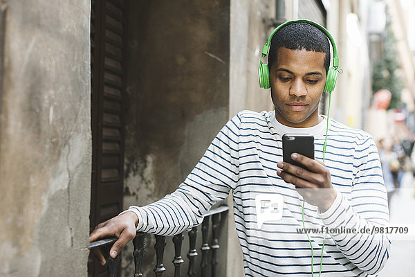 Spain  Barcelona  young man hearing music with green headphones on street