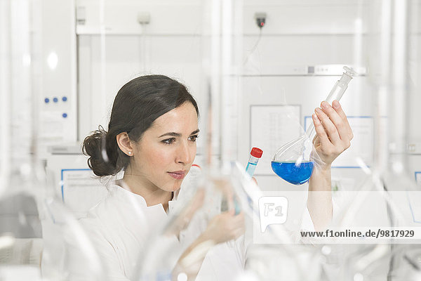 Junge Wissenschaftlerin im Labor beurteilt blaue Flüssigkeit in der Flasche