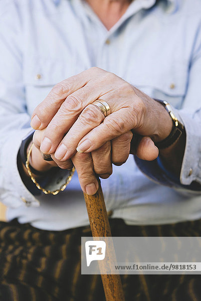 Close-up of old man's hands resting on a cane