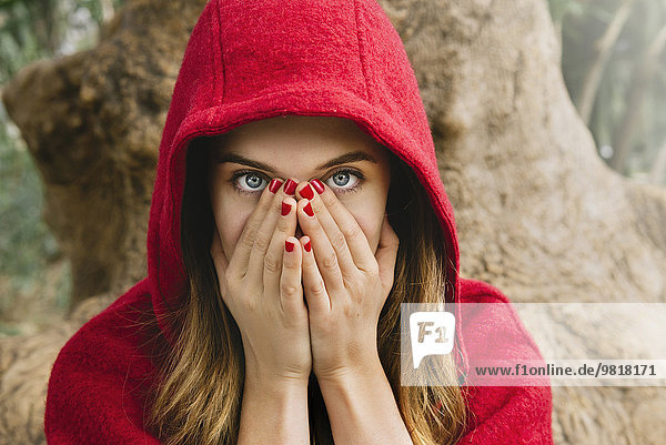 Verängstigte Frau mit roter Kapuze  die das Gesicht mit den Händen bedeckt.