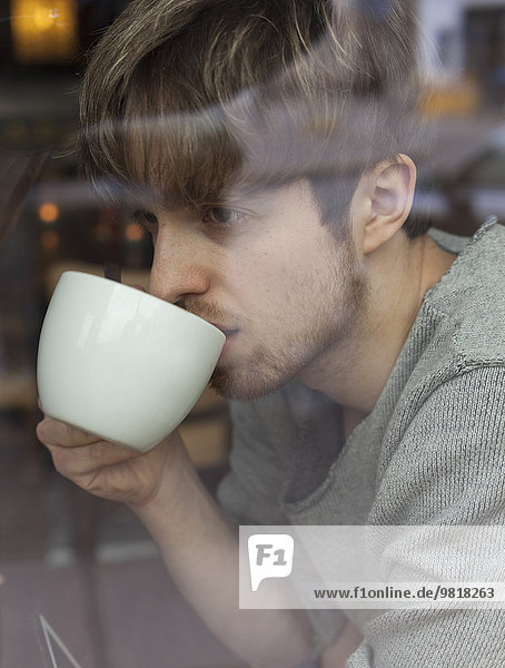 Young man behind windowpane drinking coffee