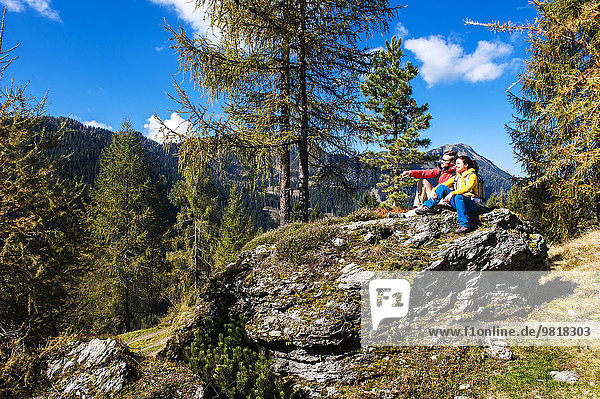 Österreich  Altenmarkt-Zauchensee  junges Paar auf einem Felsen sitzend mit Blick auf die Landschaft