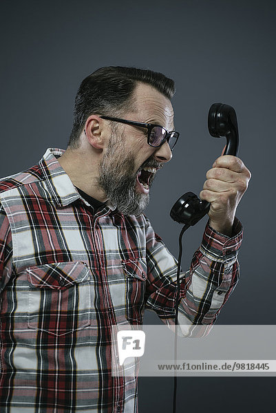 Mann schreit ins Retro-Telefon vor grauem Hintergrund