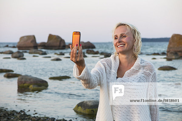 Estland  Kaesmu  blonde Frau mit einem Selfie mit Smartphone am Strand