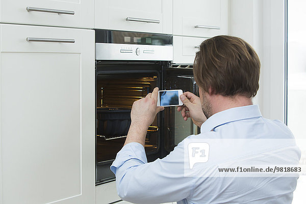 Man photographing cake in the oven with smartphone