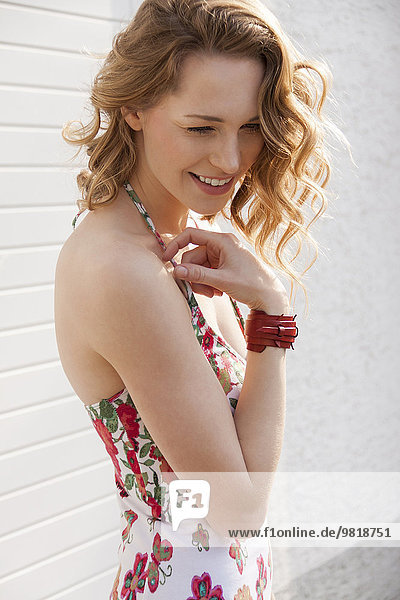 Lächelnde junge Frau mit lockigem Haar in gemustertem Sommerkleid