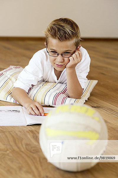 Junge macht Hausaufgaben auf Holzboden mit Blick auf Fußball