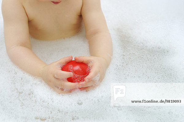 Hände des kleinen Mädchens mit rotem Ball in der Badewanne