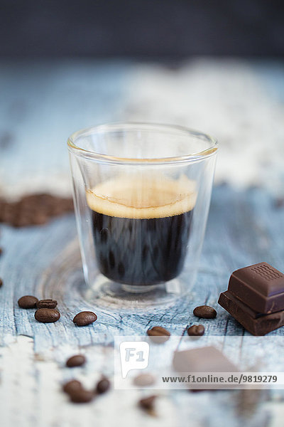 Glas Tasse Espresso  geröstete Kaffeebohnen und dunkle Schokolade auf Holz