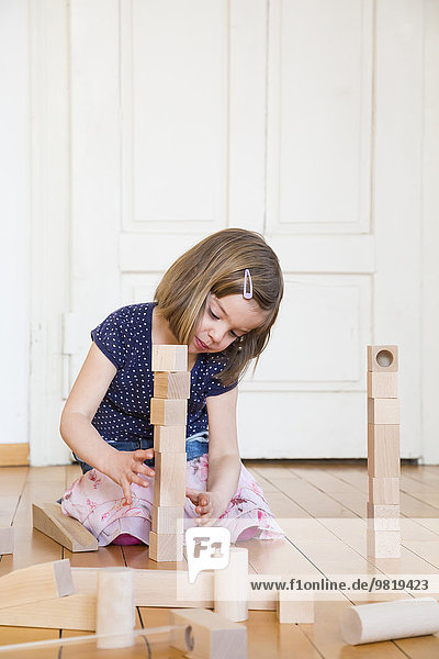 Little girl crouching on floor playing with wooden building bricks