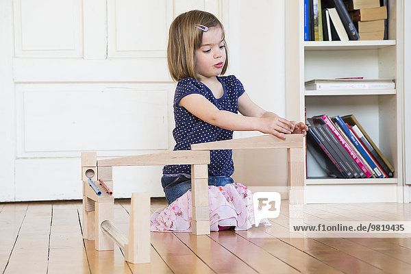 Little girl crouching on floor playing with marble run