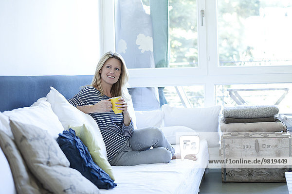 Entspannte Frau auf der Couch sitzend mit einer Tasse Kaffee