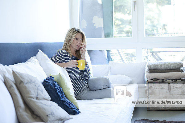 Entspannte Frau auf der Couch sitzend mit einer Tasse Kaffee