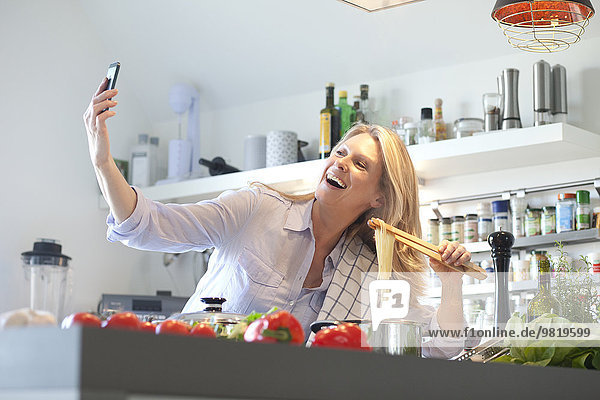 Glückliche Frau beim Kochen in der Küche mit einem Selfie