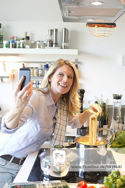 Lächelnde Frau in der Küche Kochen Spaghetti mit einem Selfie
