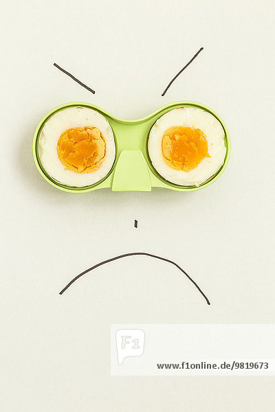 Two halves of an egg in green holder with angry face drawn around it