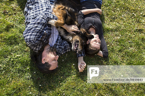 Paar mit Mischlingshund auf der Wiese liegend