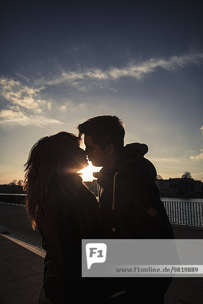 Deutschland  Berlin  Teenagerpaar beim Küssen auf einer Promenade am See
