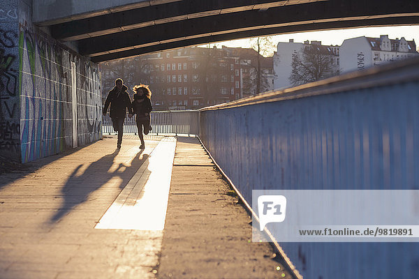 Deutschland  Berlin  Teenagerpaar unter einer Brücke bei abendlicher Sonneneinstrahlung