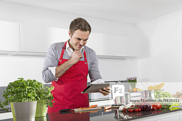 Smiling man using digital tablet while cooking