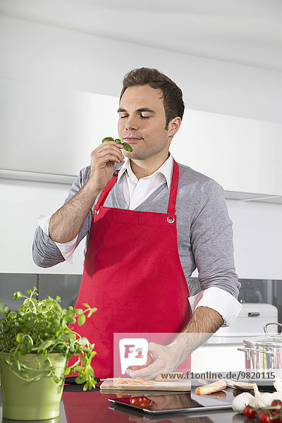 Portrait of man with red apron standing in kitchen smelling basil