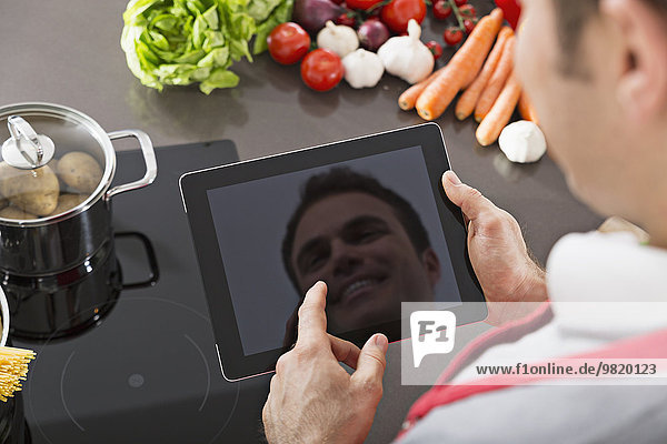 Display of digital tablet reflecting mirror image of smiling man in a kitchen