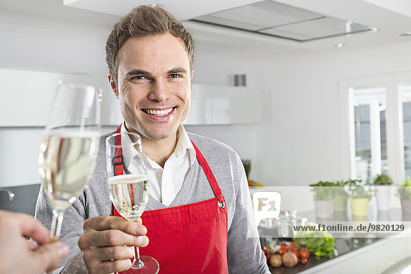 Portrait of smiling man toasting with glass of sparkling wine in kitchen