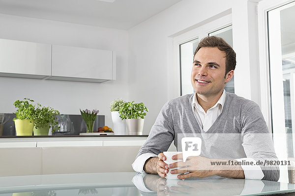 Smiling man sitting in kitchen with cup of coffee