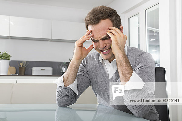 Man sitting in kitchen with hands on his face
