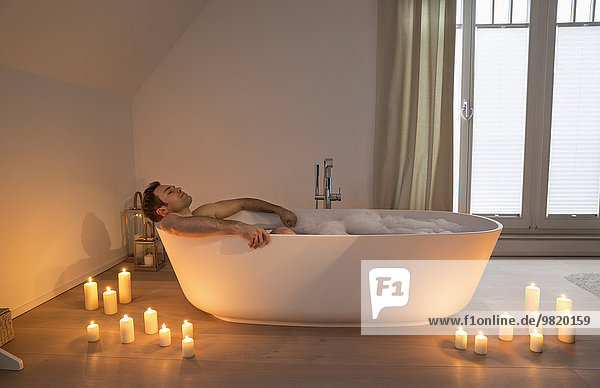 Man relaxing in bathtub with lighted candles arround