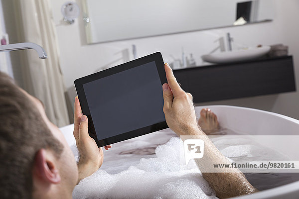 Man with digital tablet sitting in bathtub