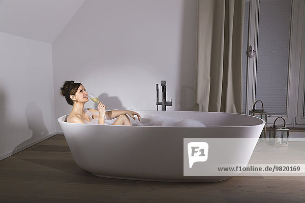 Lächelnde Frau entspannt in moderner Badewanne mit einem Glas Champagner