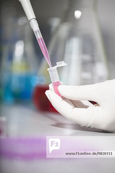 Nahaufnahme eines Wissenschaftlers der Flüssigkeit in ein Reagenzglas gießt.