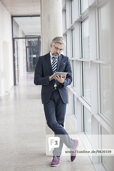Businessman leaning against column using digital tablet