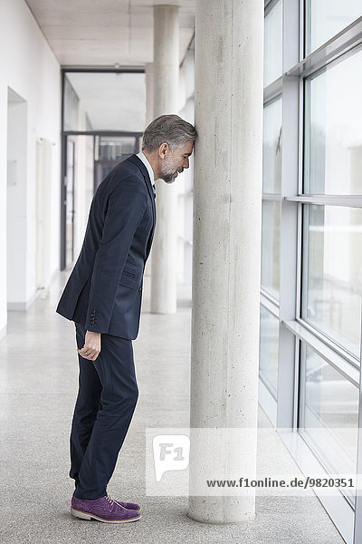 Frustrierter Geschäftsmann der sich gegen die Säule lehnt.