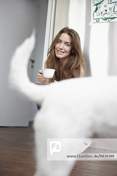 Young woman in kitchen drinking cup of coffee  dog in foreground