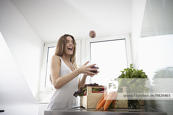 Happy young woman in kitchen with crate full of fresh vegetables