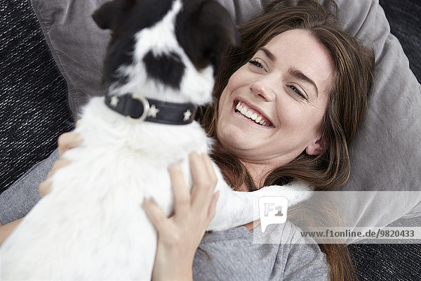 Young woman playing with dog on couch
