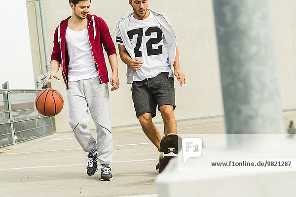Zwei junge Männer mit Skateboard und Basketball auf Parkebene