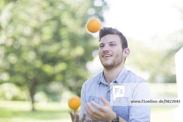 Young man juggling with oranges outdoors