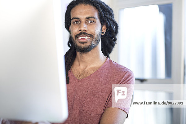 Portrait of young man with dreadlocks at desk in an office