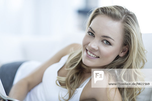 Porträt einer lächelnden blonden Frau auf einer Couch liegend