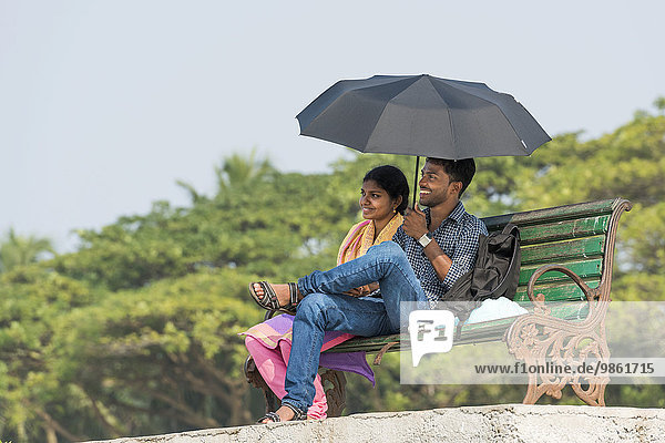 Junges Paar mit Sonnenschirm auf einer Parkbank  Fort Kochi  Kerala  Indien  Asien