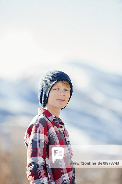 A boy with a woolly hat and checked shirt standing in open countryside in winter.
