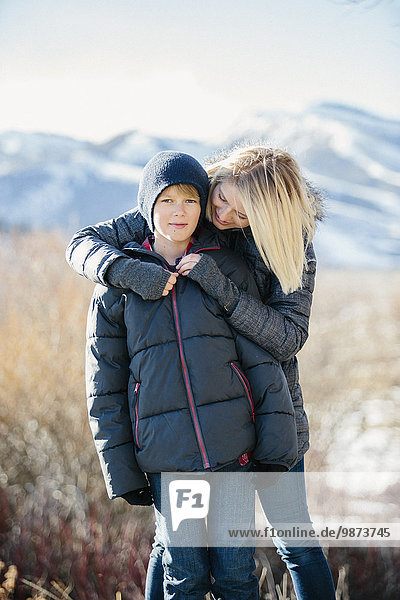 A boy in a jacket and woolly hat being hugged by his mother.