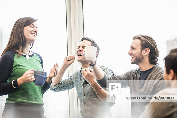 Vier Arbeitskollegen machen eine Pause  lachen und erheben ihre Kaffeetassen.